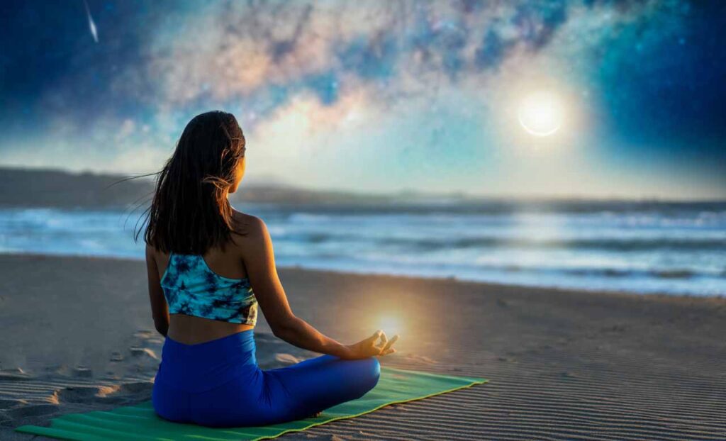 woman meditating at night in the beach, in the background the milky way and moon with shooting star